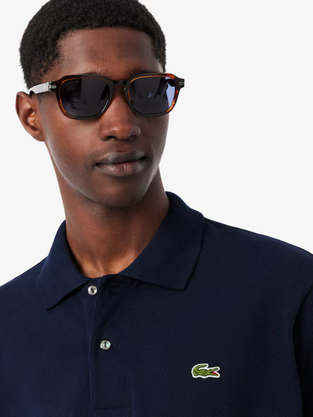 Man wearing sunglasses and a navy polo shirt with a green logo.